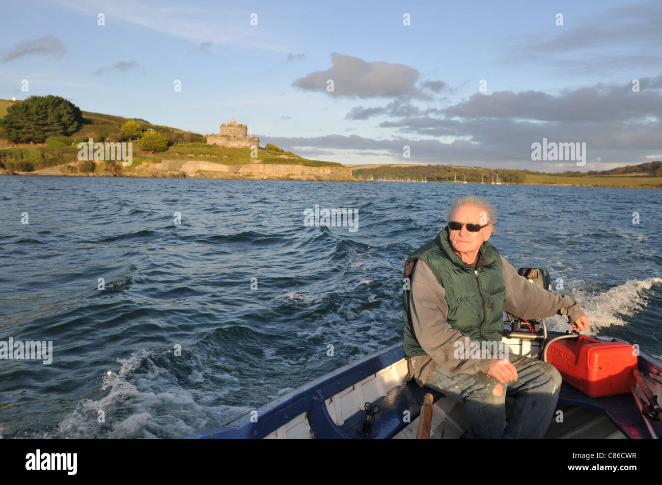 Un uomo nella sua metà degli anni sessanta entra Falmouth Harbour nella sua barca dopo un viaggio di pesca con St Mawes castello in background. Foto Stock