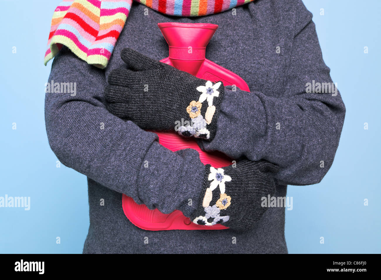 Foto di una donna tenendo un red hot bottiglia d'acqua per il suo torace indossando kniited mano guanti di lana cercando di tenere in caldo Foto Stock