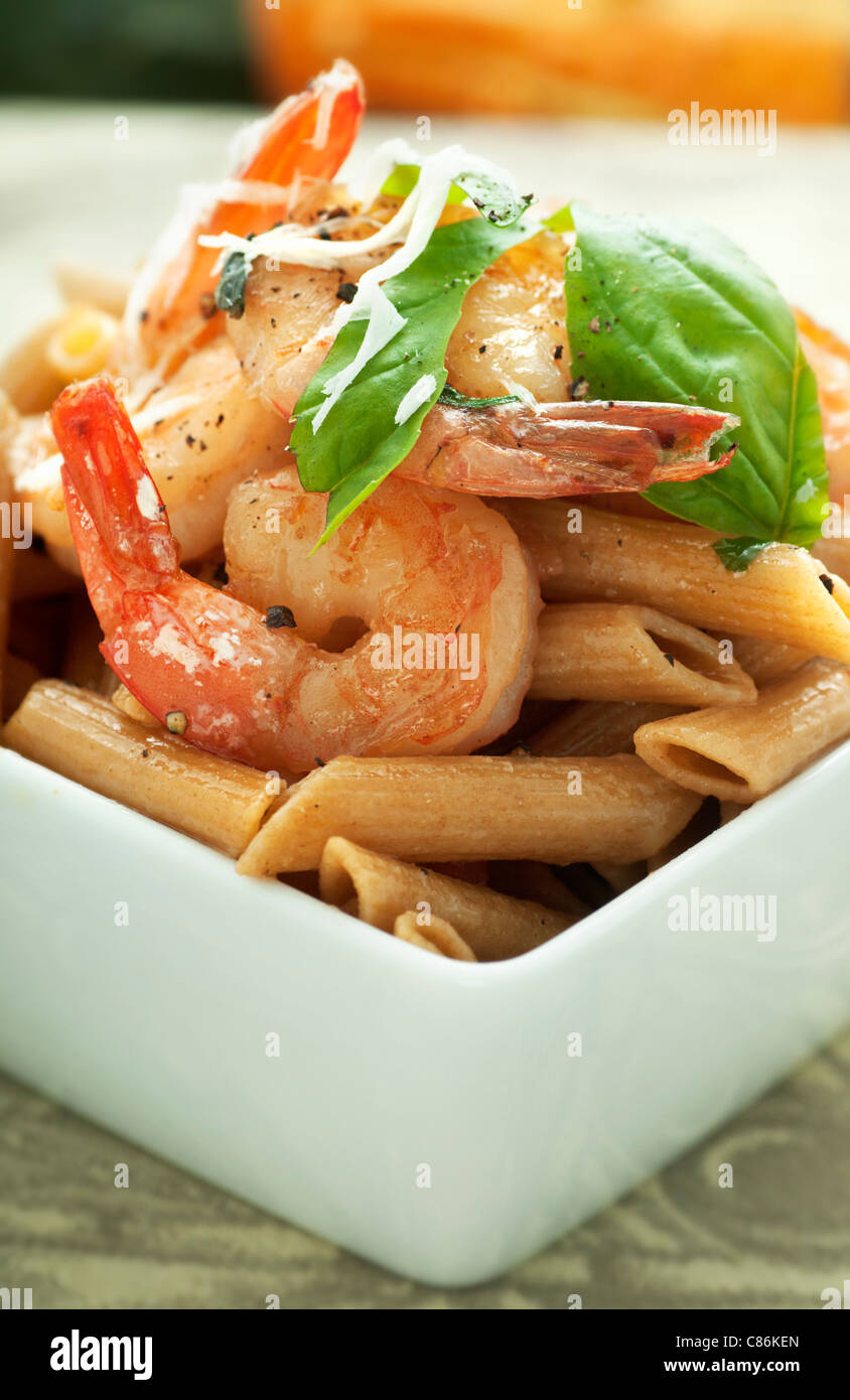 Quadrato bianco ciotola di grano intero penne pasta con gamberi saltati e basilico Foto Stock