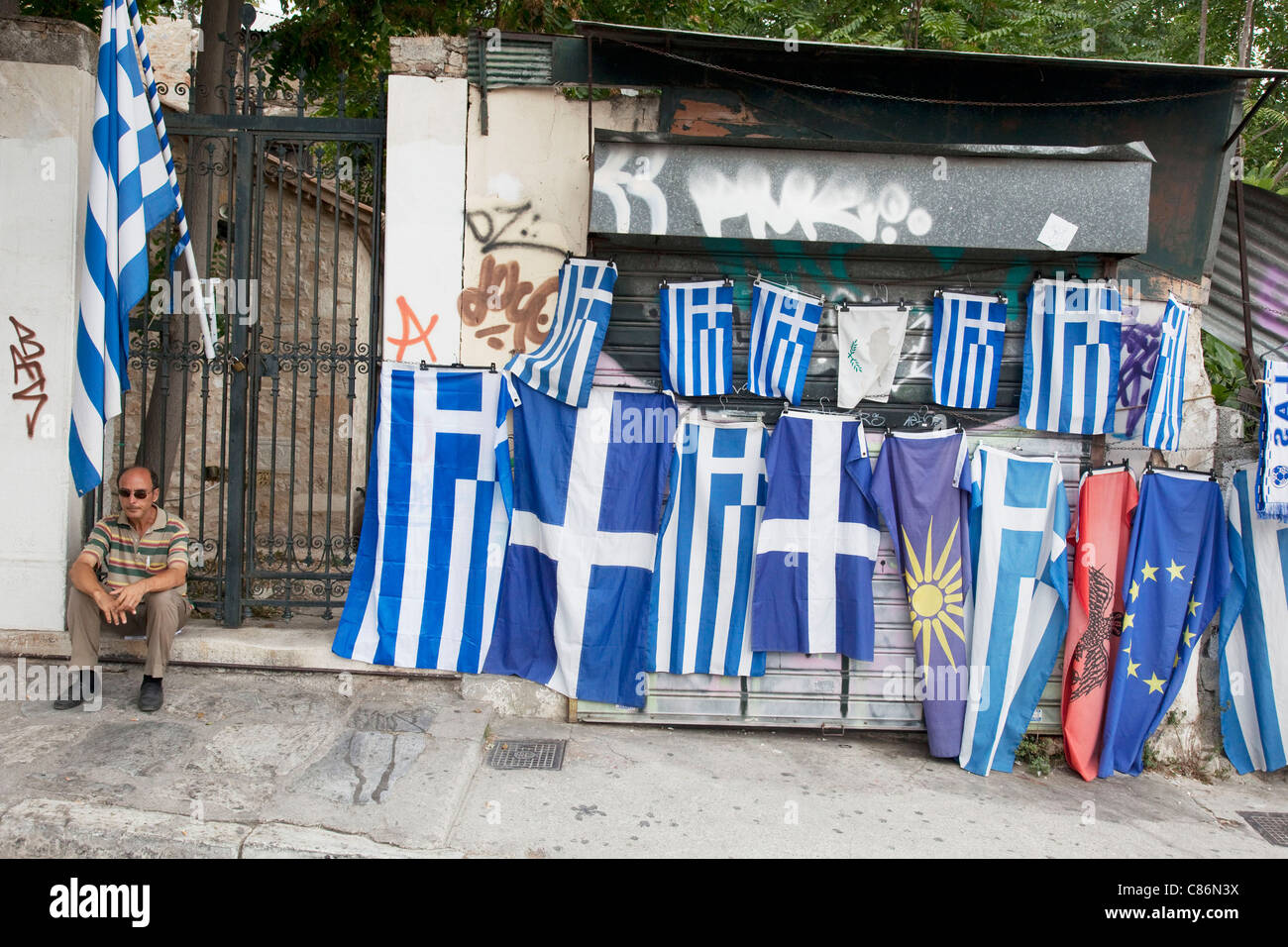 Scena di strada nel quartiere di Plaka, un uomo con le bandiere Greca per la vendita. Plaka è il vecchio quartiere storico di Atene, Grecia. Foto Stock