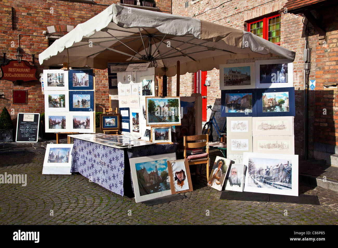 Una bancarella vendendo souvenir tourist stampe, dipinti e bozzetti in Huidevetters Plein o i conciatori' Square, Bruges, Belgio Foto Stock