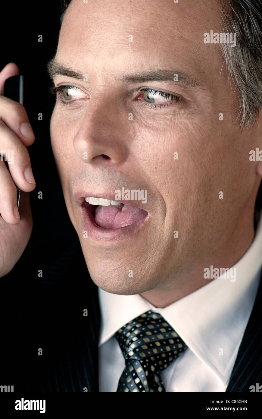 Un imprenditore ha una conversazione sul suo telefono cellulare mentre lo sta guardando con incertezza nervoso. Foto Stock