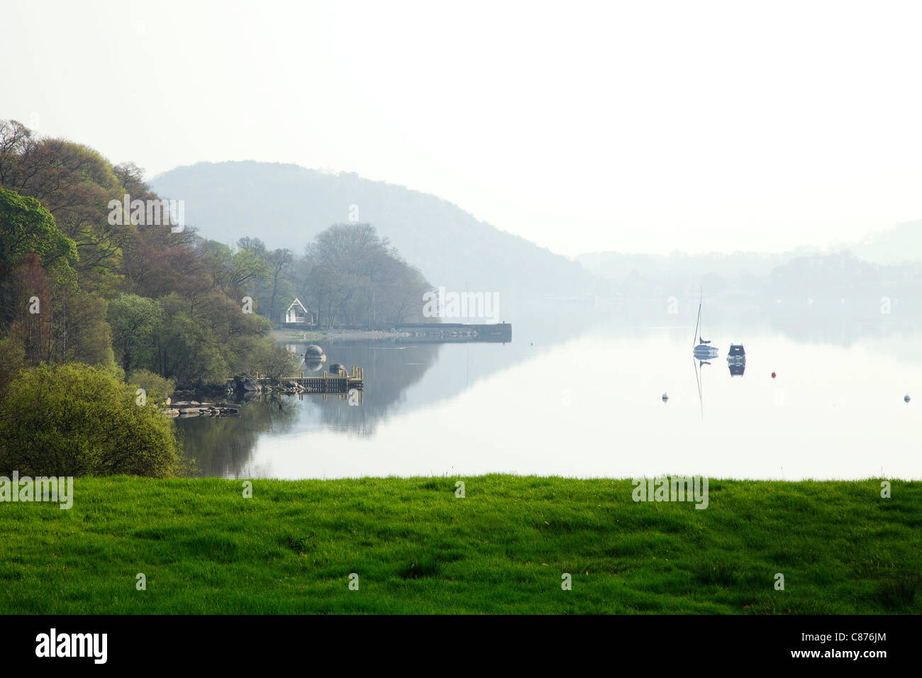 Ullswater lago all'alba con barche e riflessi e nebbia pesante Foto Stock