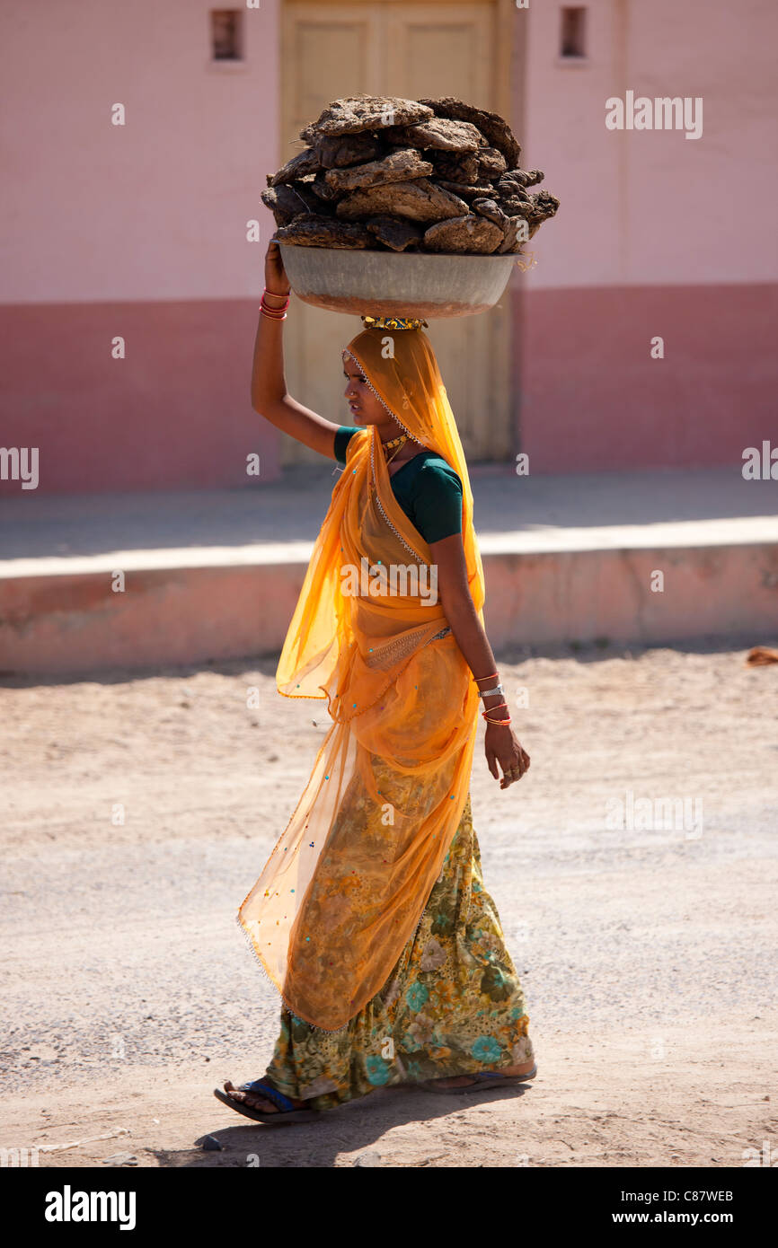 Donna indiana in sari che trasportano sterco di vacca panetti a secco per combustibile di cottura a Khore villaggio in Rajasthan, India settentrionale Foto Stock
