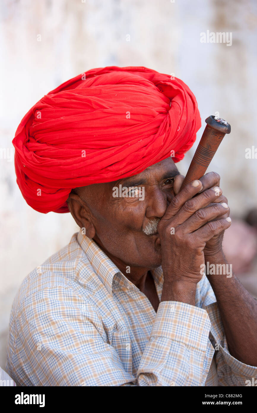 Indian uomo indossa turbante di Rajasthani fuma tradizionale tubo di argilla in Narlai village nel Rajasthan, India settentrionale Foto Stock