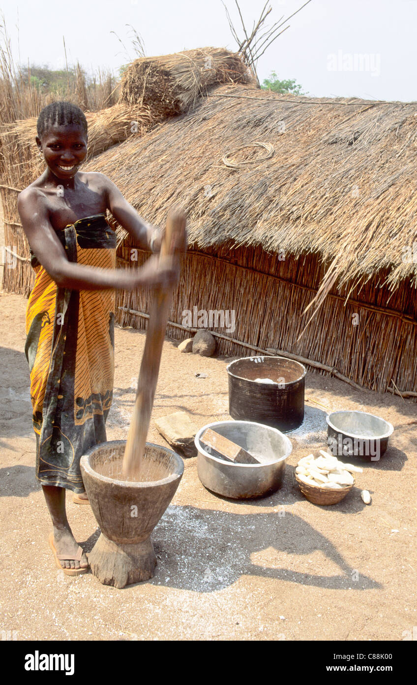 Kipili, Tanzania. Ragazza sorridente pounding manioca in una ciotola di legno con pestello stick. Foto Stock