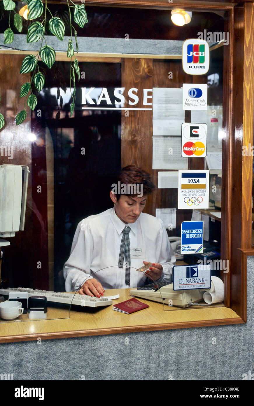 Budapest, Ungheria. Valuta Exhange luogo; donna che guarda ad una carta bancaria seduto dietro la finestra; computer sulla scrivania. Foto Stock