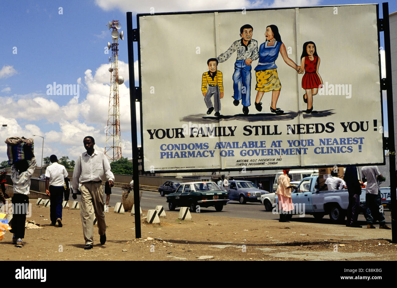 Lusaka, Zambia, Africa. Poster Anti-Aids accanto ad una strada trafficata con relè di telecomunicazioni torre dietro. Foto Stock