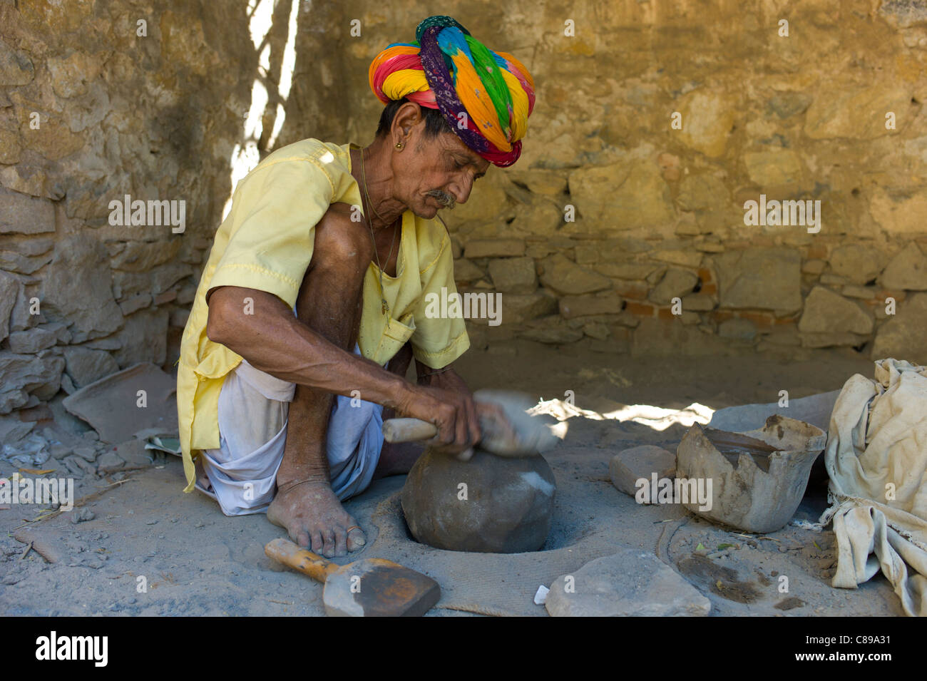 Indian potter nel tradizionale turbante di Rajasthani lavora a casa la preparazione di argilla nel villaggio di Nimaj, Rajasthan, India settentrionale Foto Stock