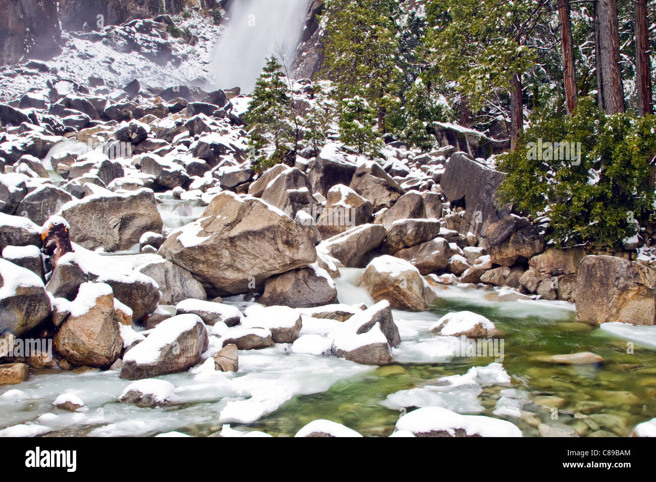 Acqua vorticazione tramite coperta di neve rocce alla base di Yosemite Falls Foto Stock