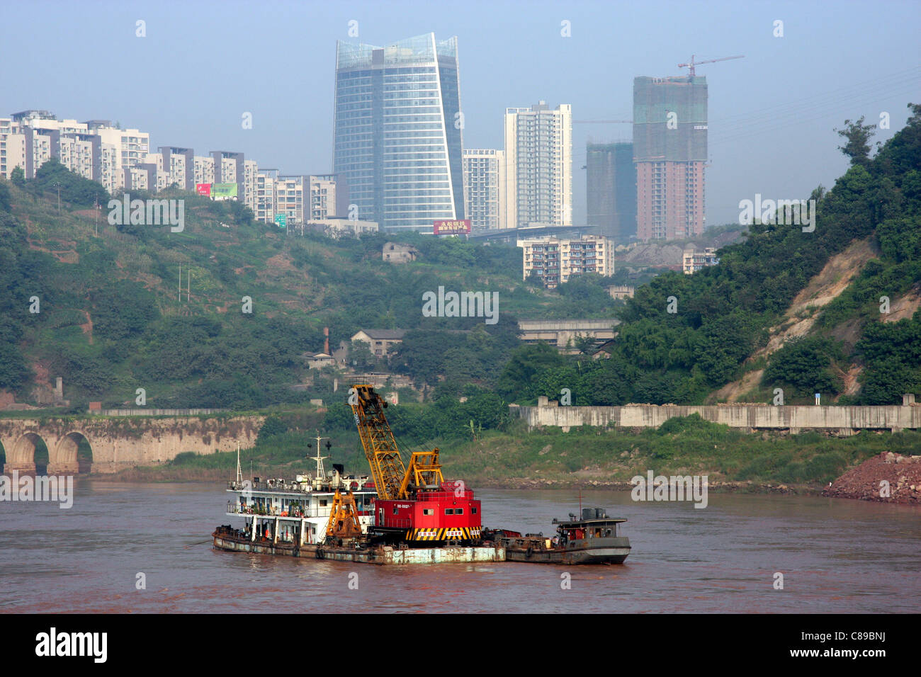 Skyline della città e una grande clam shell dragare sul Fiume Yangtze a Chongqing Cina Foto Stock