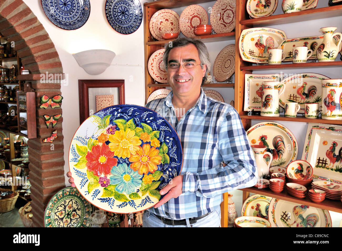 Portogallo Alentejo: proprietario di un negozio di Amilcar mostra raditional piastra ceramica nel suo negozio di souvenir 'Mufla' in Monsaraz Foto Stock