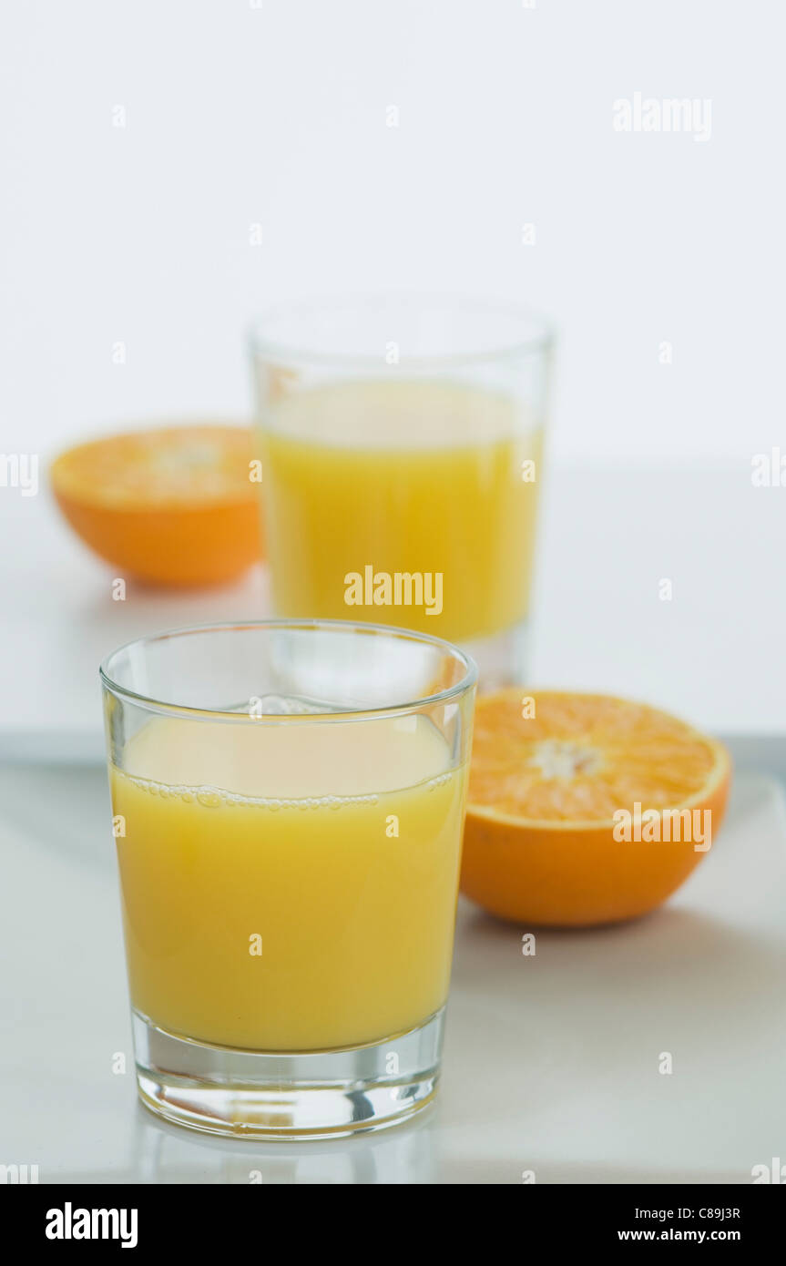 Bicchieri di succo d'arancia con metà arance sul tavolo Foto Stock