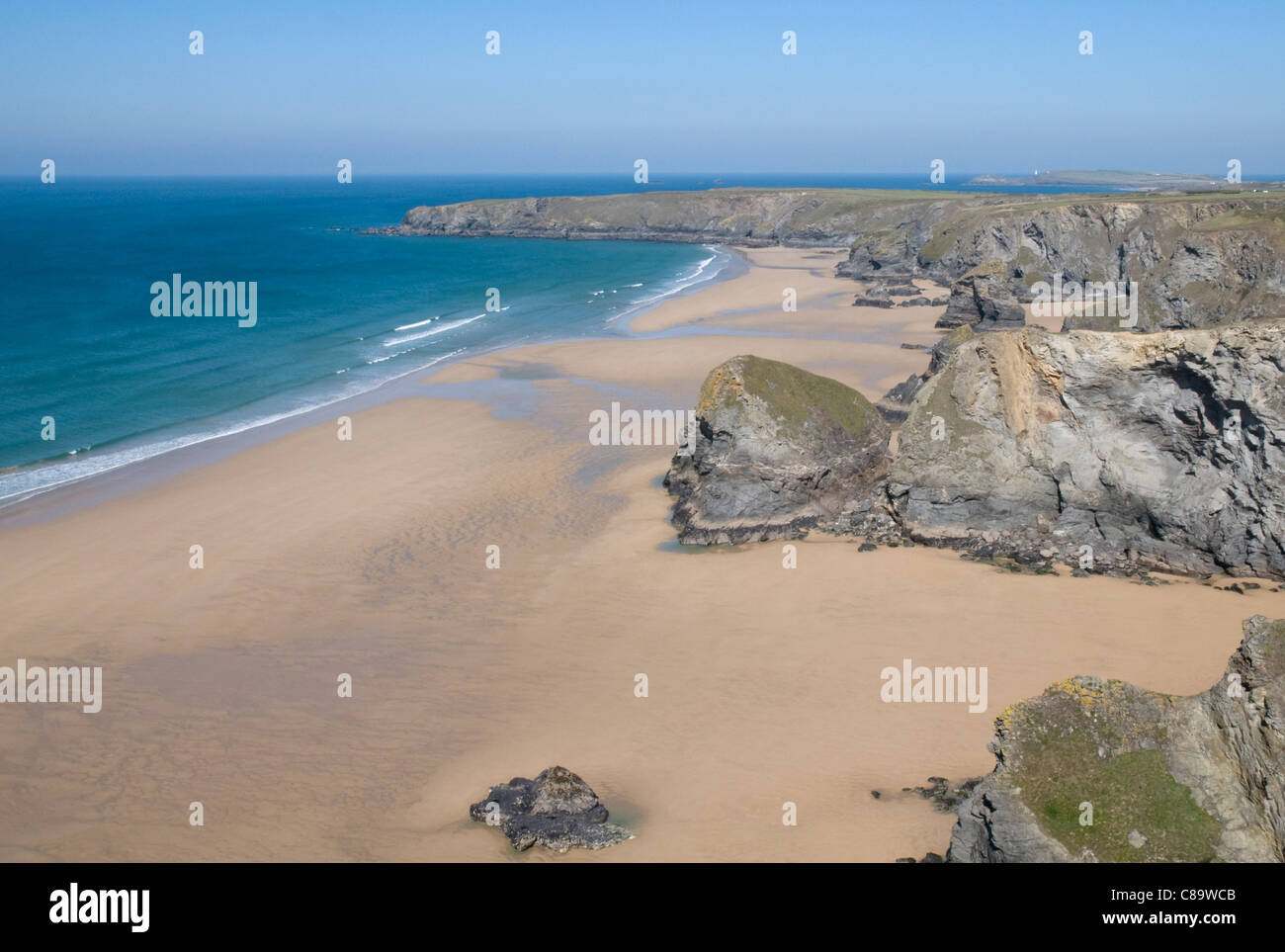 La bassa marea espone una vasta distesa di sabbia dorata a Bedruthan Steps, con parco in testa la distanza. Foto Stock