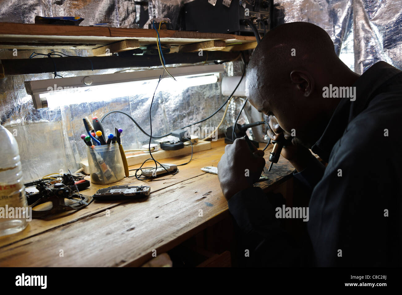 Un giovane uomo che lavora in un telefono mobile repair shop, Thika, Kenya. Foto Stock