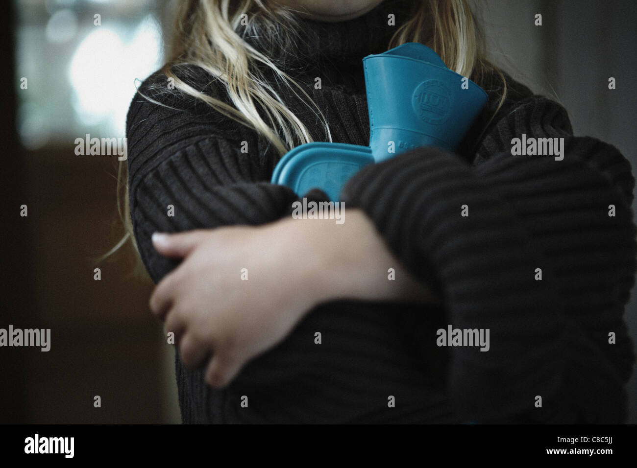 Una chiusura di una giovane ragazza con una boule dell'acqua calda e indossando un ponticello di grandi dimensioni Foto Stock