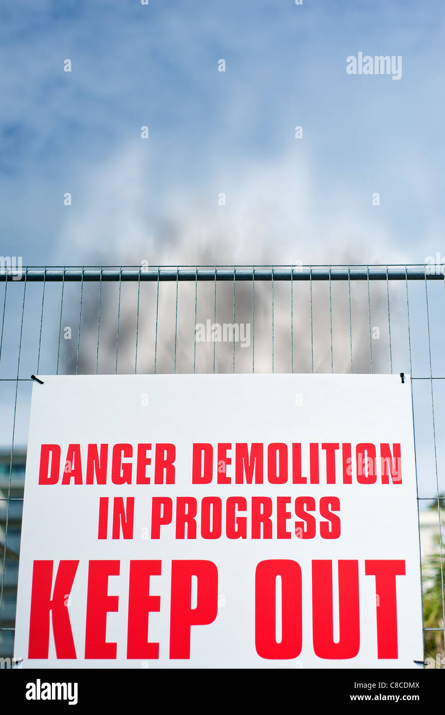 Segno attaccato al recinto lettura ' pericolo demolizione in corso tenere fuori ' con l'aumento del fumo dietro di esso. Foto Stock