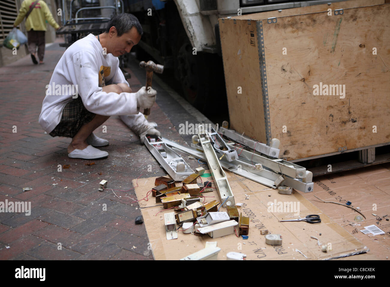 Sulla strada deposito di riciclaggio in Kowloon, Hong Kong, Cina. Un lavoratore si rompe i componenti elettrici a vendere per rottami Foto Stock