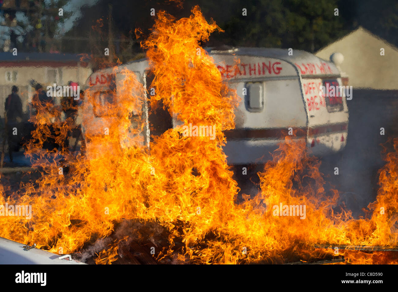 Un fuoco fiammeggiante nella parte anteriore di una roulotte che è stata verniciata con slogan di protesta durante la Dale Farm sfratti in Essex. Foto Stock