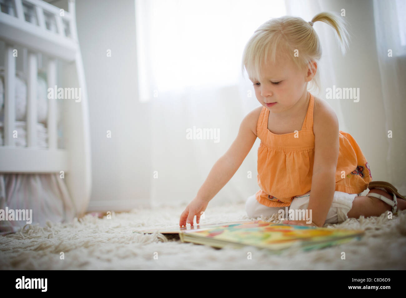 Il Toddler ragazza seduta sul pavimento guardando Picture Book Foto Stock