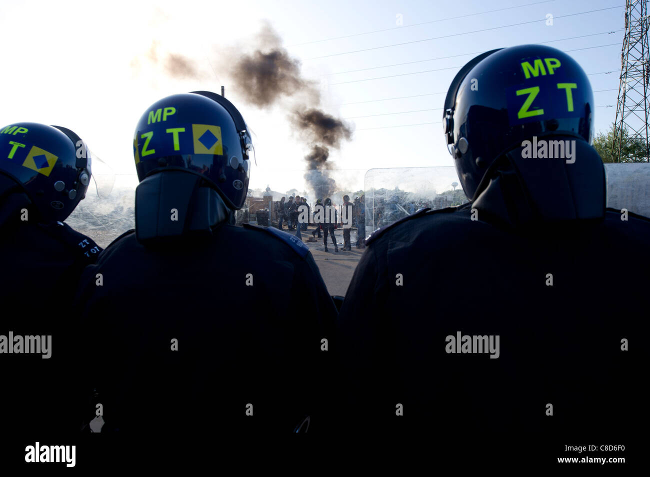 Dale Farm lo sfratto. Riot tre funzionari di polizia sul cordone di manifestanti come impostare gli incendi su il viaggiatore del sito come il fumo aumenta. Foto Stock
