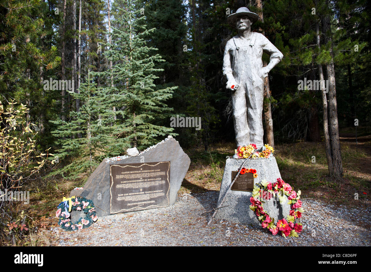 Statua e lapide commemorativa di un uomo circondato da corone colorate in un ambiente forestale presso il Castle Mountain Internment Camp, Banff National Park. Foto Stock