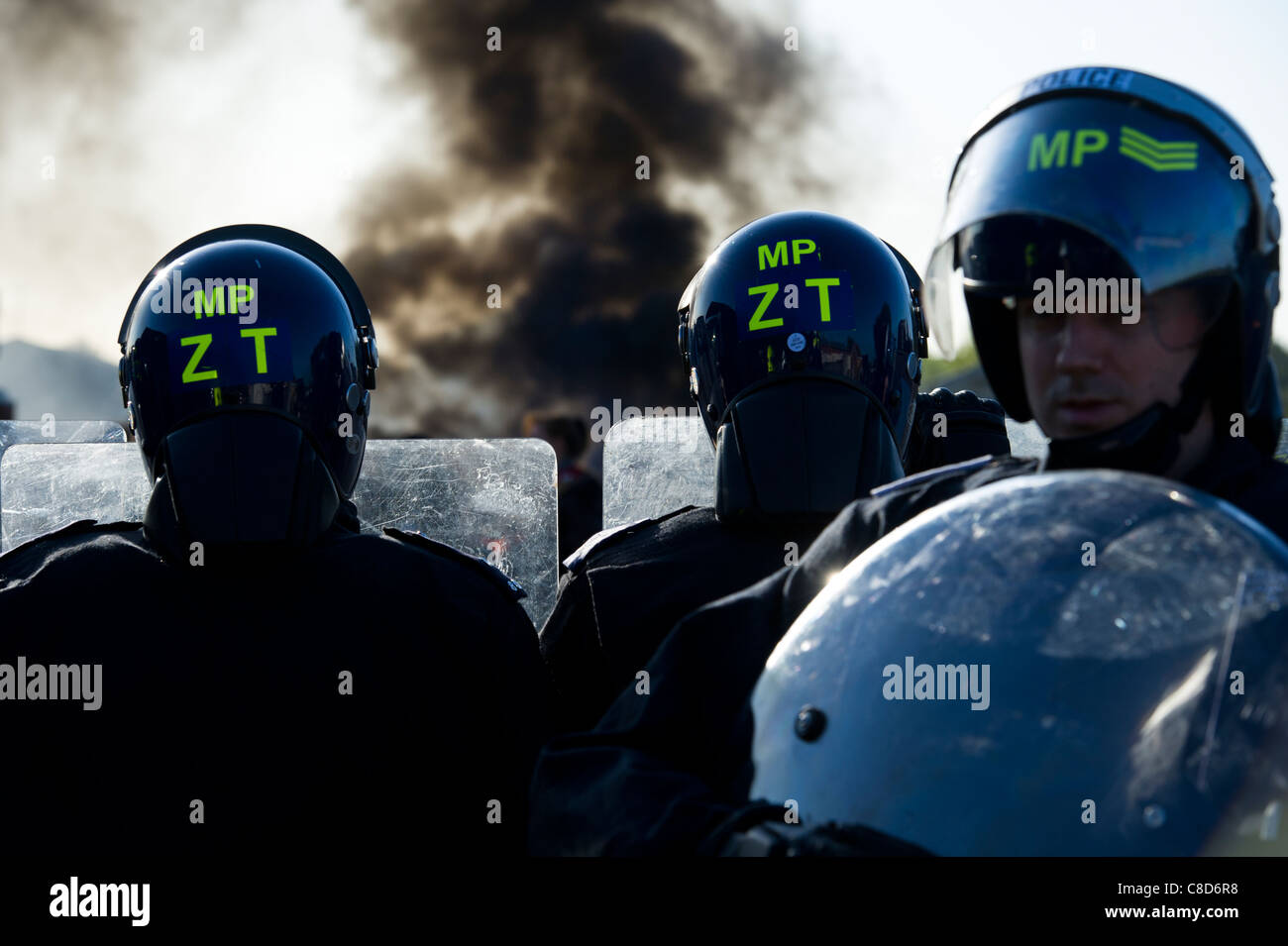Dale Farm lo sfratto. Riot tre funzionari di polizia sul cordone di manifestanti come impostare gli incendi su il viaggiatore del sito come il fumo aumenta. Foto Stock