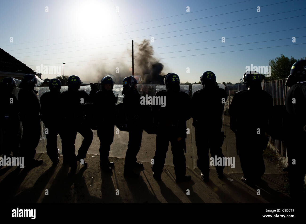 Una linea di sommossa funzionari di polizia con i loro scudi formando un cordone attraverso la strada su un sito zingaro durante un sfratto forzato. Foto Stock
