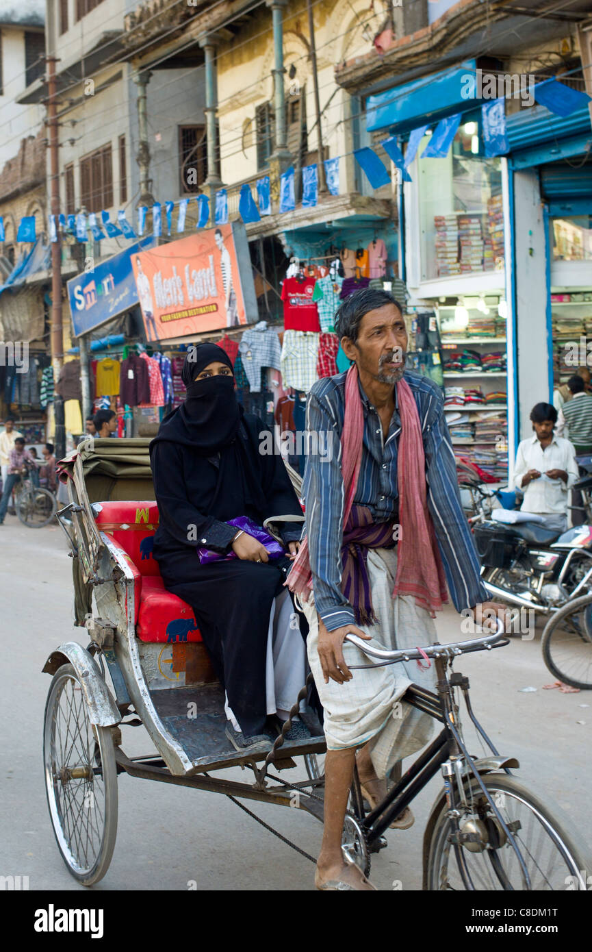 Scena di strada nella città santa di Varanasi, giovane donna musulmana in black burkha giostre in rickshaw, Benares, India settentrionale Foto Stock