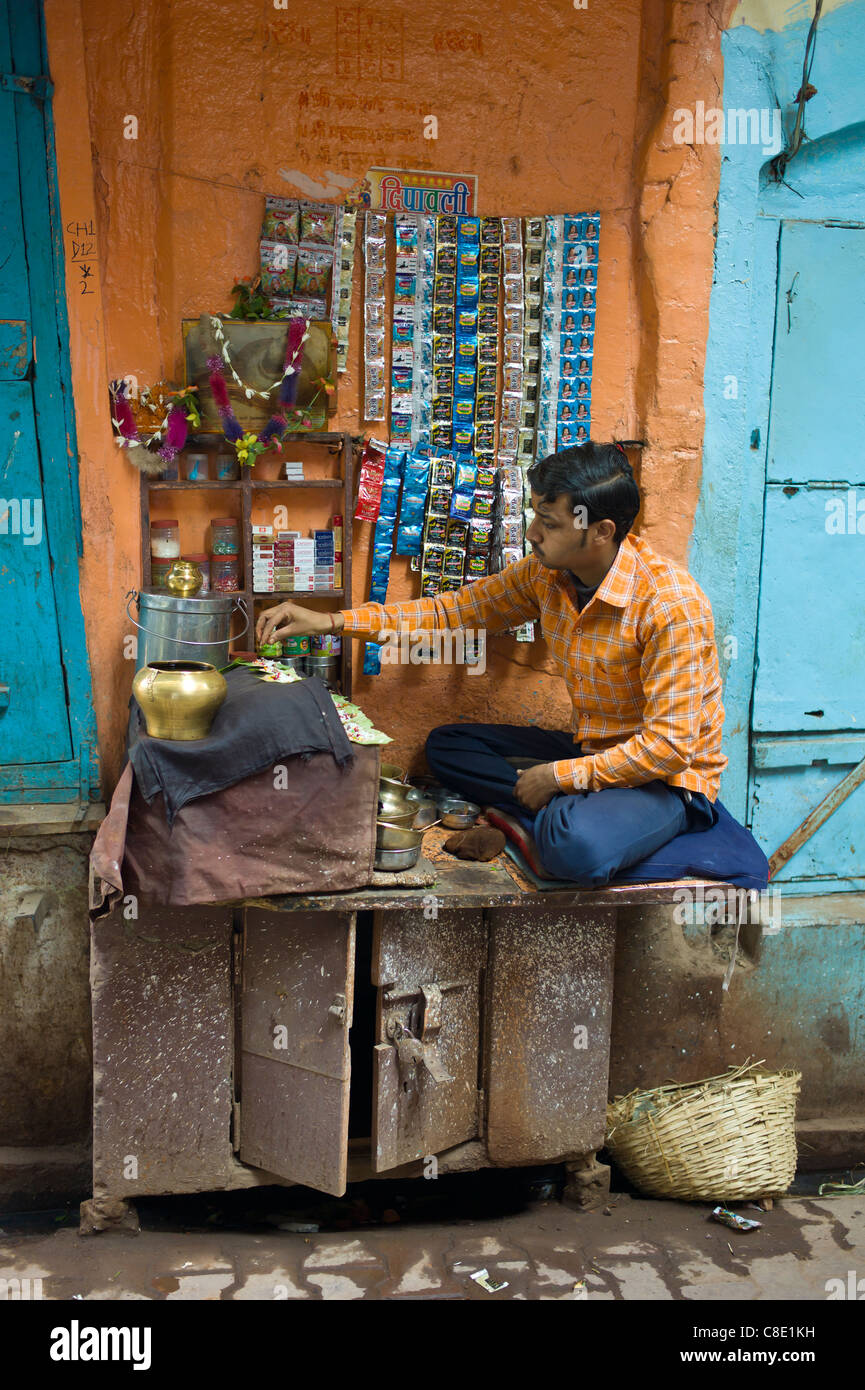 Indian l'uomo corre il mercato in stallo vicoletto nella città di Varanasi, Benares, India settentrionale Foto Stock