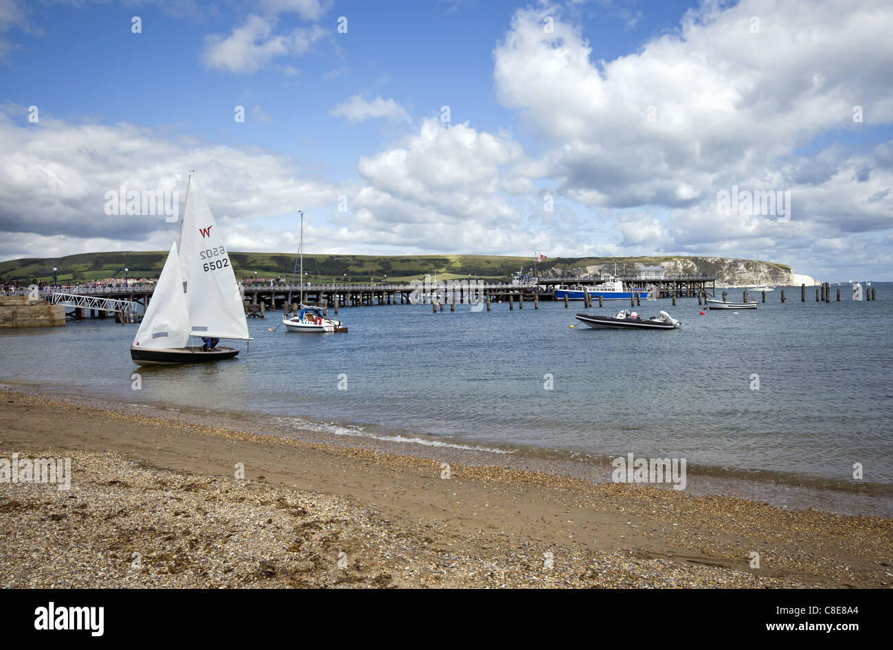 Barche a vela a Swanage bay con il molo e Ballard punto nella distanza. Il Dorset, England, Regno Unito Foto Stock