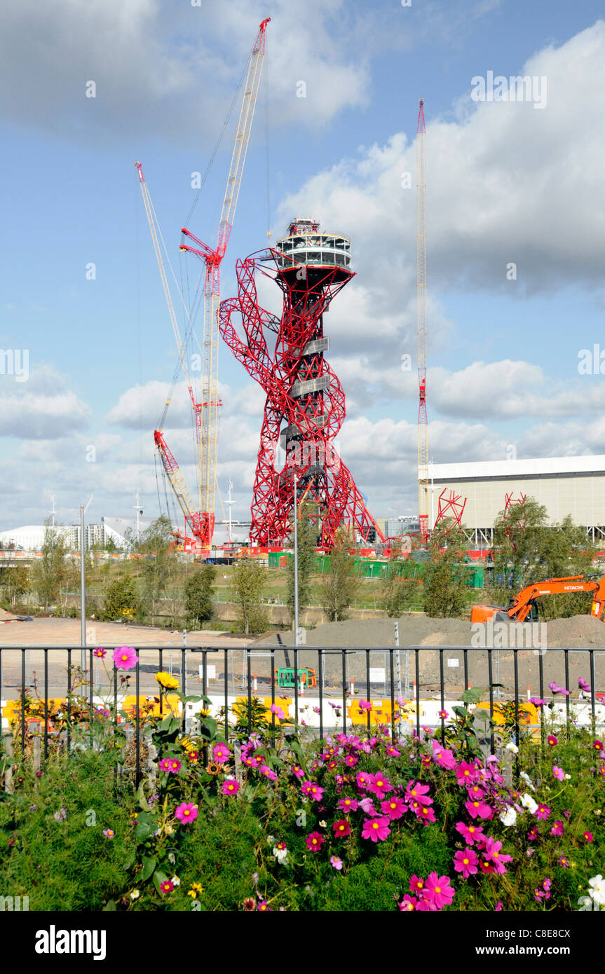 Display floreali lungo la greenway percorso con una parte di Londra 2012 Olympic sito in costruzione di gru i lavori in corso in materia di ArcelorMittal Orbit tower Stratford Foto Stock