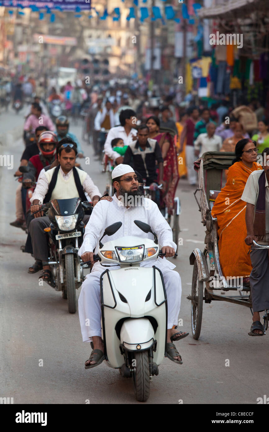 Uomo musulmano indossando topi cappello e vestito di bianco motore scooter in scena di strada nella città di Varanasi, Benares, India settentrionale Foto Stock