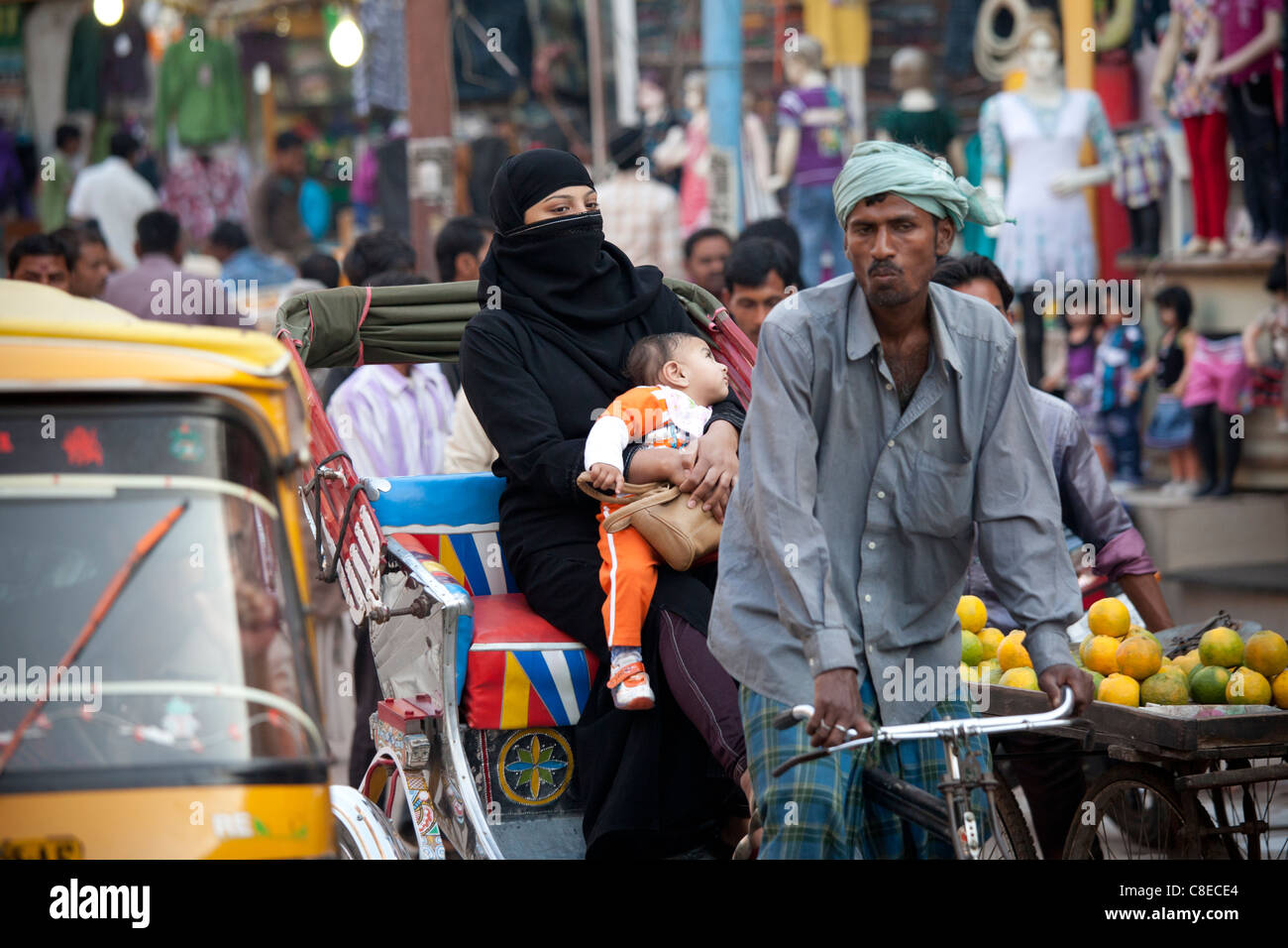 Donna musulmana e il bambino viaggia in rickshaw in strada affollata scena nella città di Varanasi, Benares, India settentrionale Foto Stock