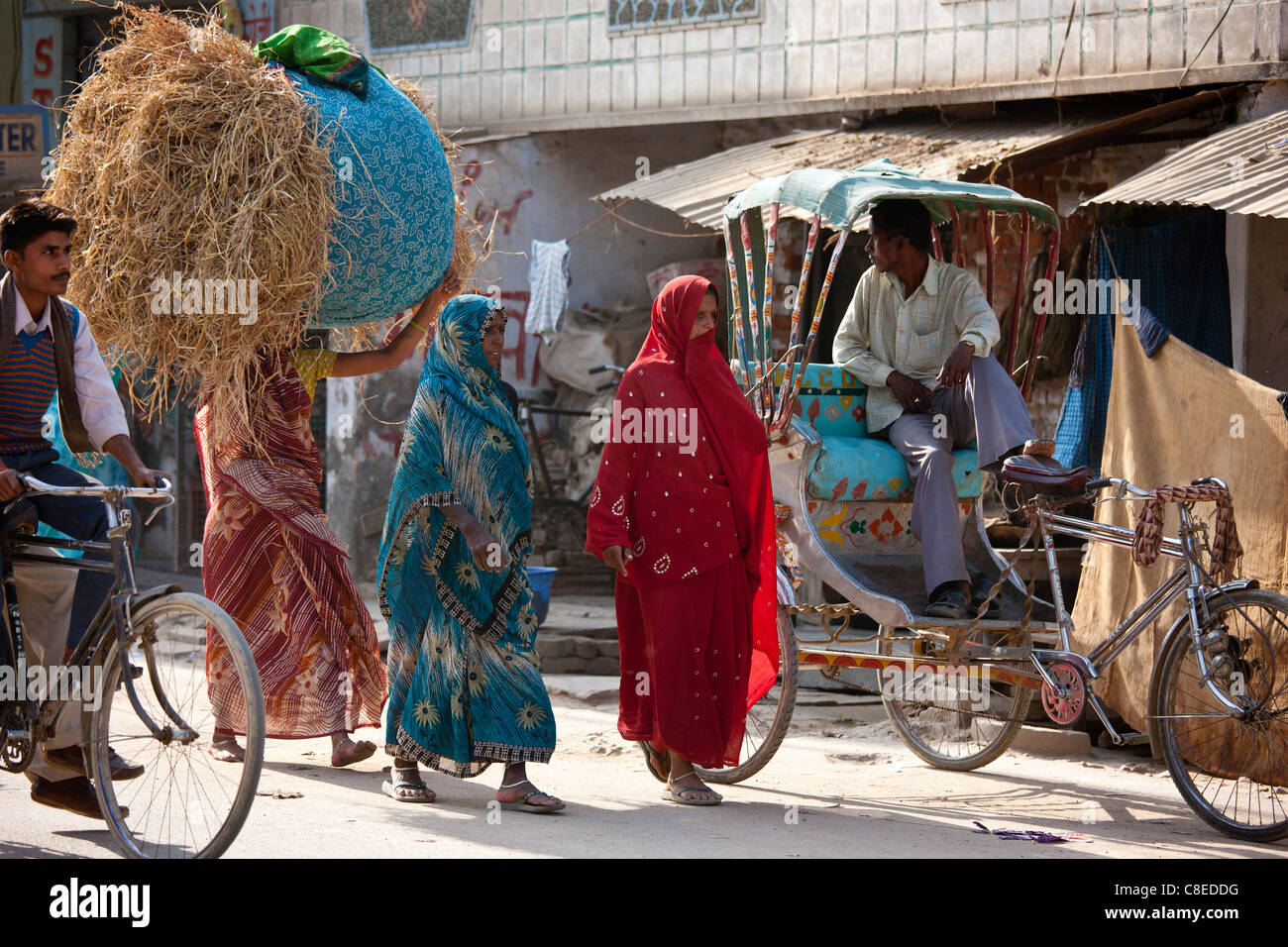 Le donne indiane a piedi in strada, uno portante delle balle di paglia sulla testa, in Nandi vicino a Varanasi, Benares, India settentrionale Foto Stock