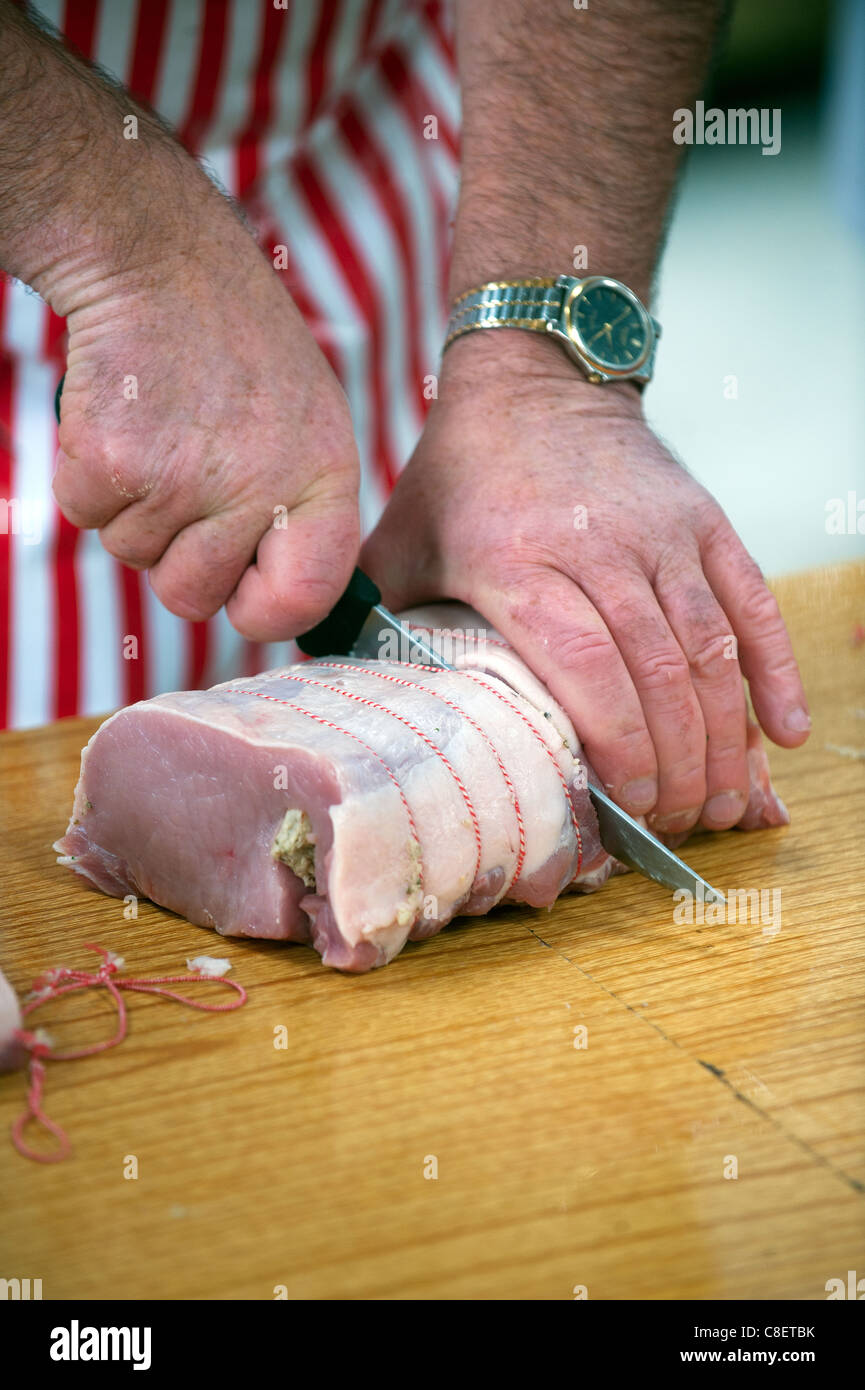Un macellaio taglia un giunto disossata di maiale. Foto Stock