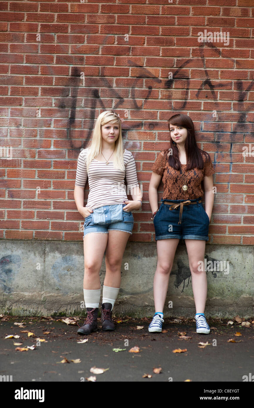 Due annoiati cercando 16 17 anni, ragazze adolescenti, in piedi di fronte a un muro di mattoni, REGNO UNITO Foto Stock