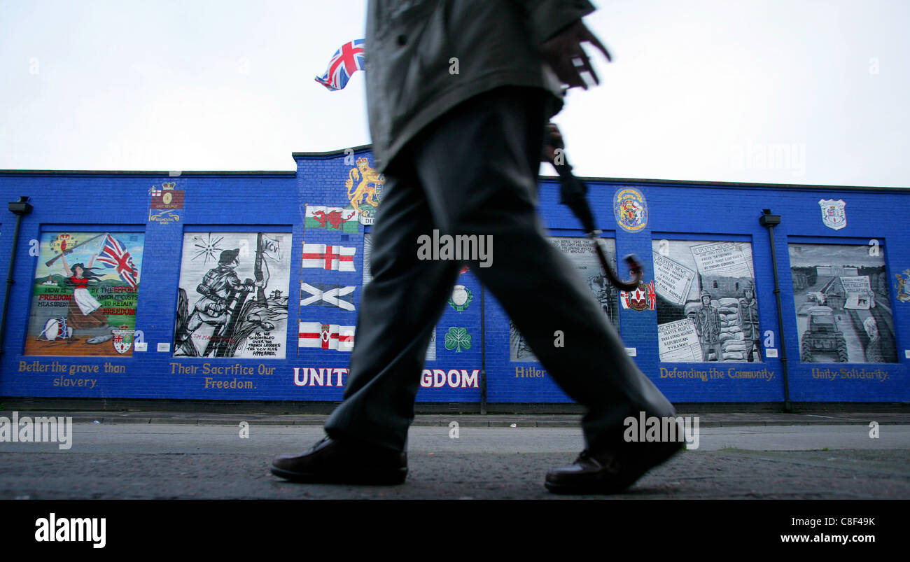 Un uomo cammina passare un murale lealisti nell'streetsof sabbiosa area di riga a Belfast, Irlanda del Nord Foto Stock