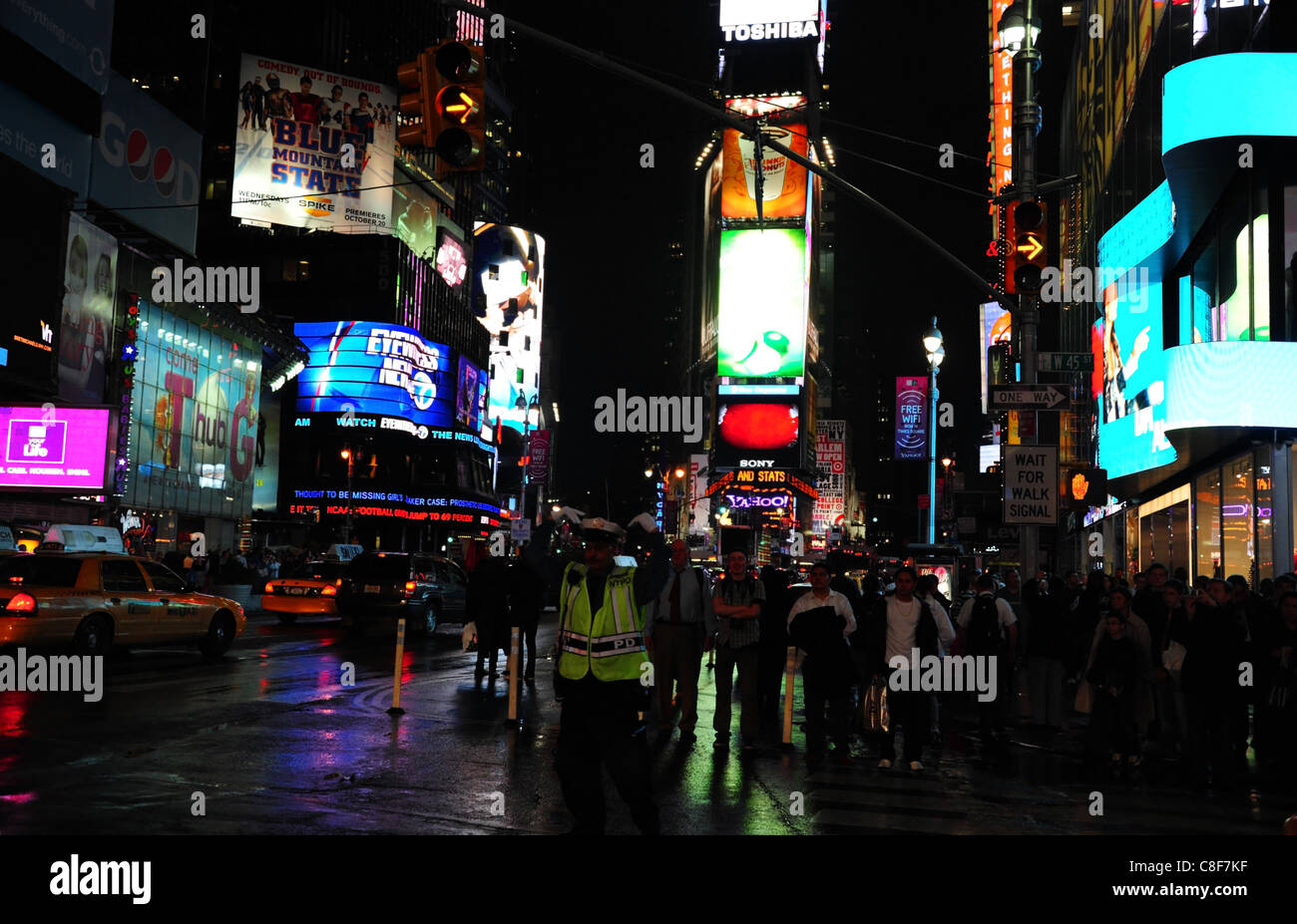 Night Shot poliziotto che dirige il traffico neon umido asfalto persone attraversando Road, West 45th Street 7th Avenue, Times Square, New York Foto Stock