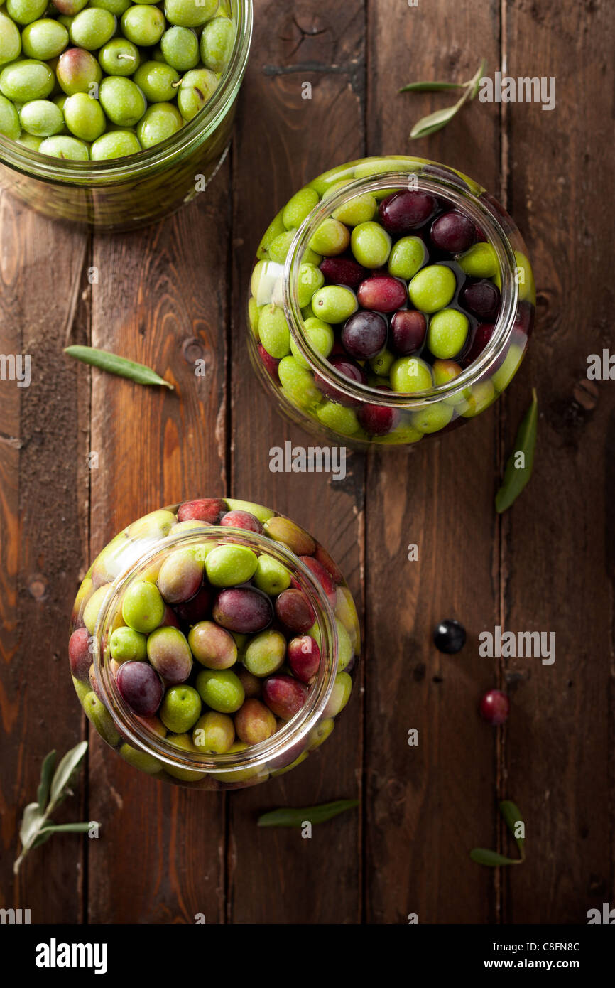 Olive in salamoia (con acqua e con acqua e sale in vasi di vetro) su legno Foto Stock