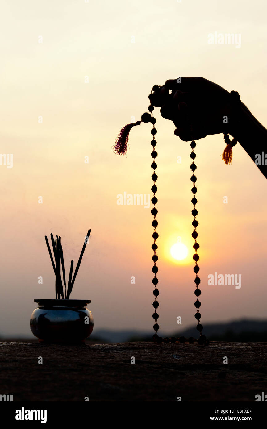 Man mano utilizzando Rudraksha indiano / Japa Mala i grani di preghiera e di incenso . Silhouette Foto Stock
