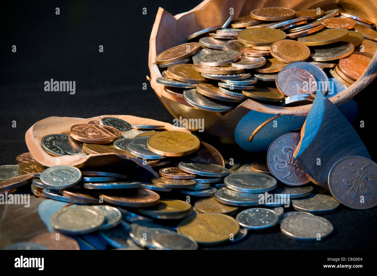 Rotto il risparmio terramundi pot con denaro fuoriuscita sopra il tavolo contro uno sfondo nero Foto Stock