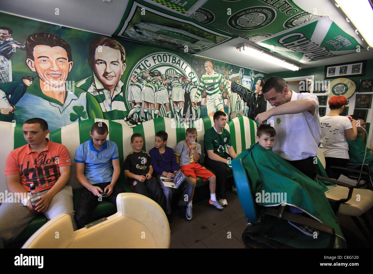 Un giovane ragazzo riceve un taglio di capelli con Celtic di gioco del calcio (calcio) murales dietro di lui. Foto Stock