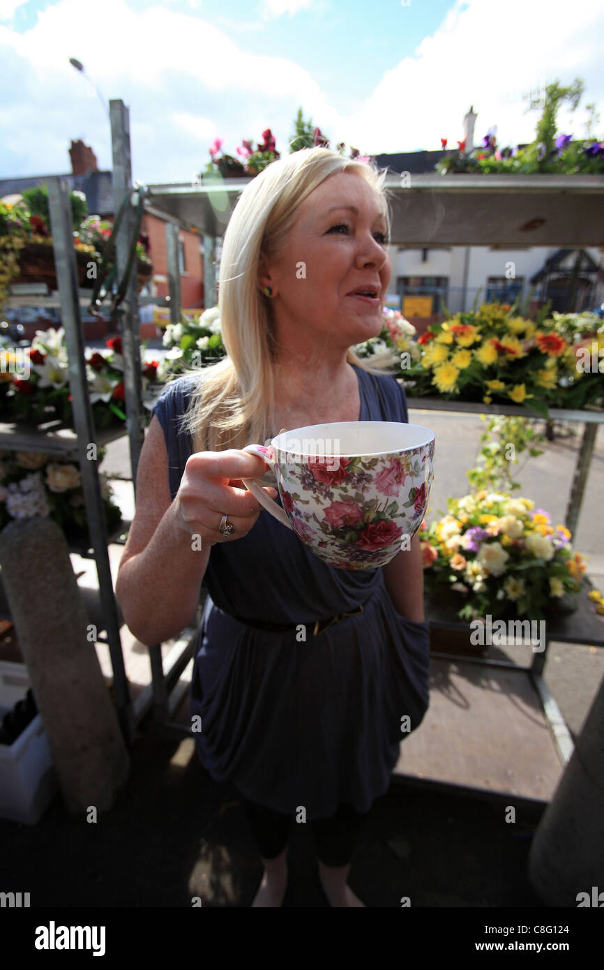 Una donna sorrisi come ella beve una tazza di caffè al di fuori di un negozio di fiori a Belfast, Irlanda del Nord Foto Stock