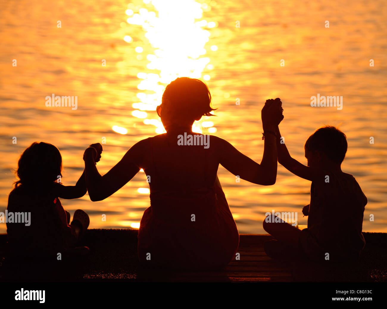 Profili della madre e bambini contro il mare scintillante al tramonto Foto Stock