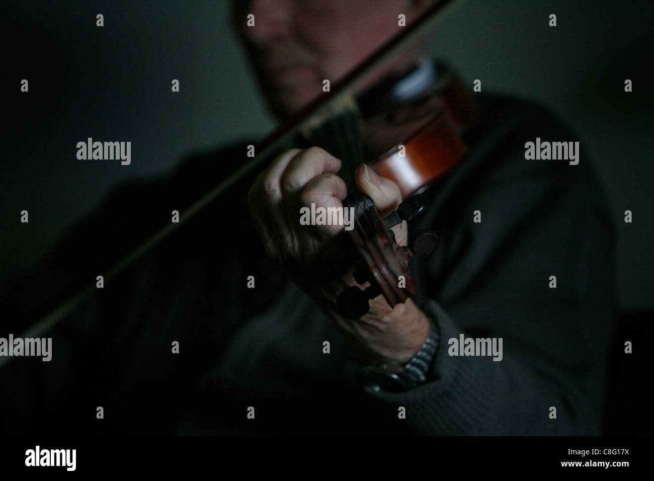 Un maschio maturo la riproduzione di musica irlandese sul violino in una stanza buia Foto Stock