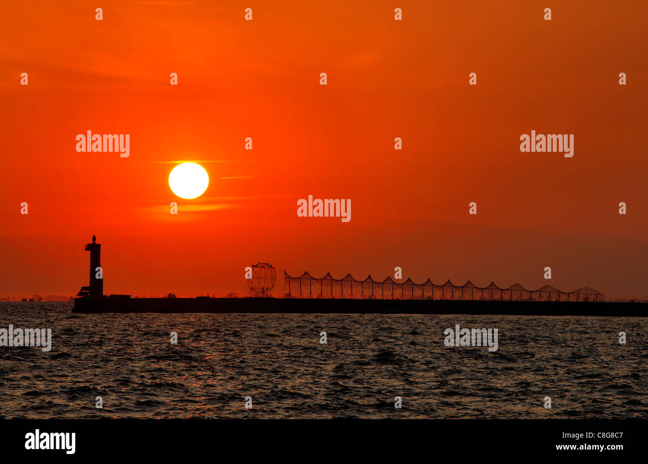 Un'installazione artistica e il faro del molo del porto di Salonicco, al tramonto. Macedonia, Grecia. Foto Stock