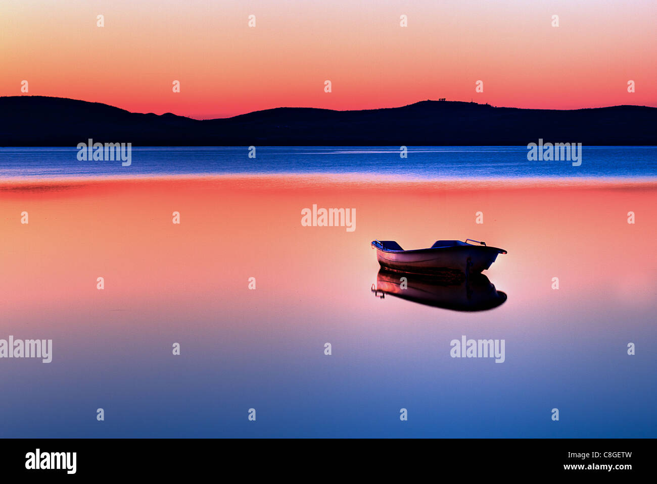 Vista panoramica di piccole barche da pesca in acque calme al tramonto con le colline in background. Foto Stock