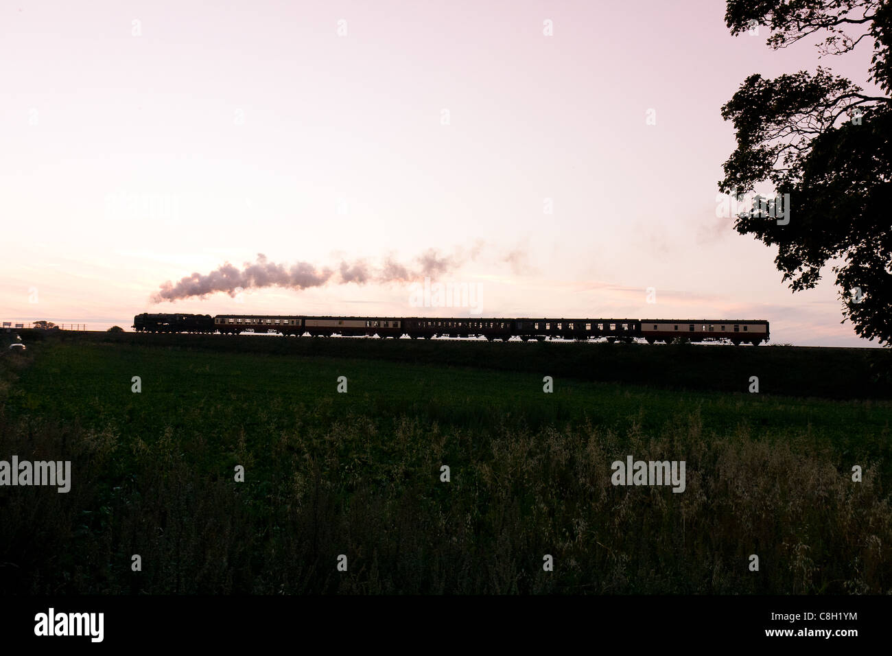 Locomotiva a vapore la trazione di un treno passeggeri sulla North Norfolk Railway al tramonto Foto Stock