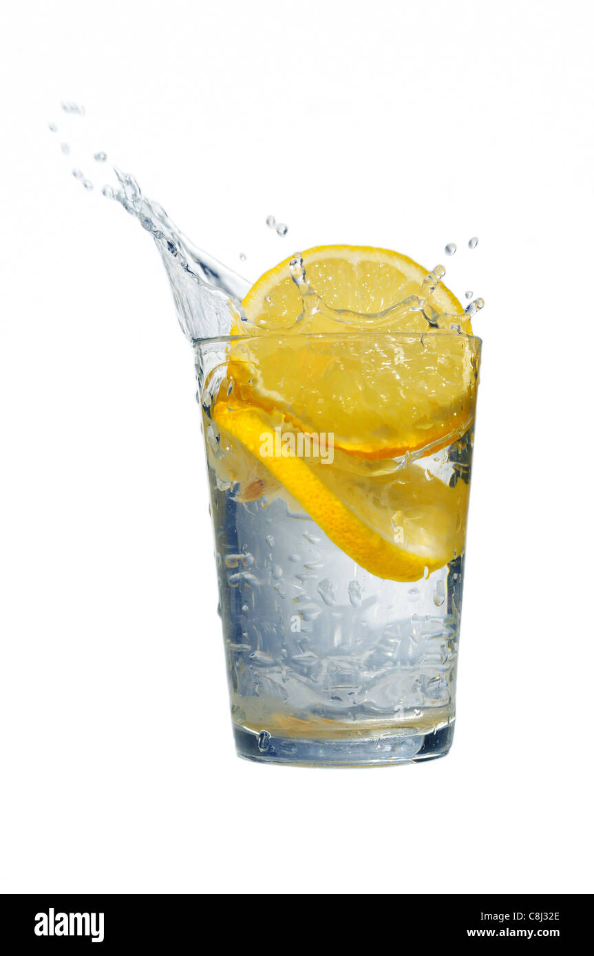Un bicchiere di acqua fresca con la caduta di limoni isolato su bianco Foto Stock
